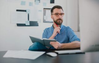 Nachdenklicher Mann mit Notizbuch sitzt am Schreibtisch in seinem Büro