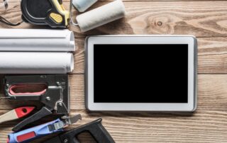 Tablet neben Werkzeugen, Bauplänen und Farbrolle auf einer Holzwerkbank