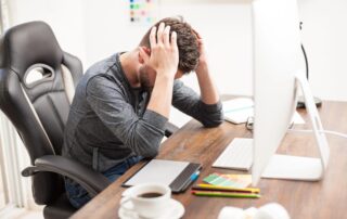 Verzweifelter Mann sitzt am Schreibtisch und hält sich den Kopf