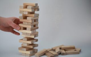 Hand zieht einen Holzklotz aus einem wackligen Turm